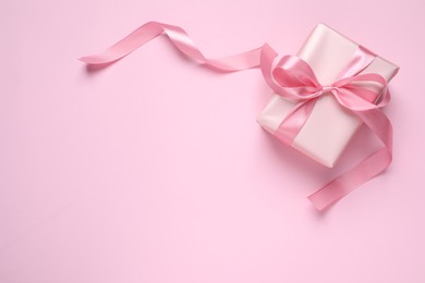 Beautiful gift box with bow on pink background, top view. Space for text