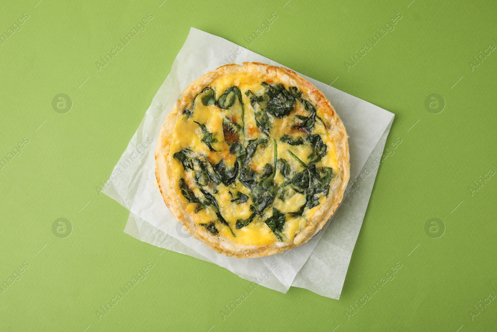 Photo of Delicious pie with spinach on green background, top view