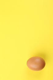 Raw chicken egg on yellow background, top view. Space for text