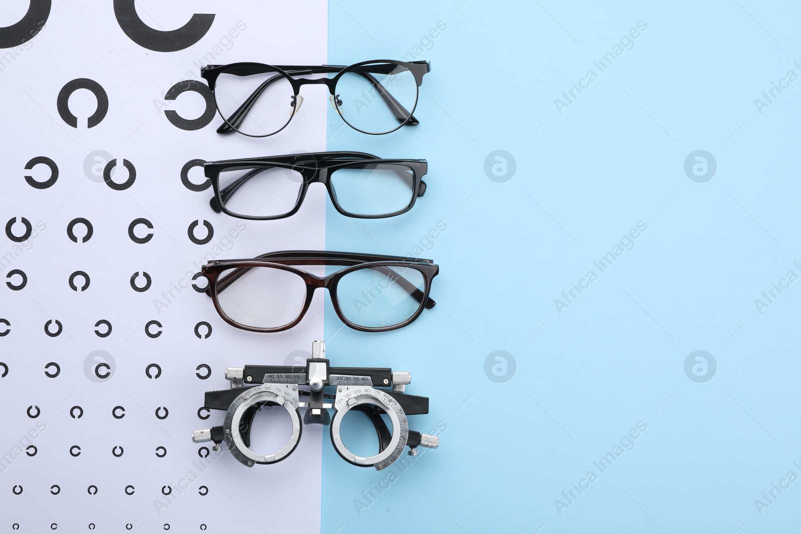 Photo of Vision test chart, glasses and trial frame on light blue background, flat lay. Space for text