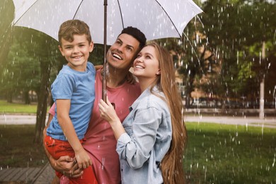 Photo of Happy family with umbrella walking under rain in park
