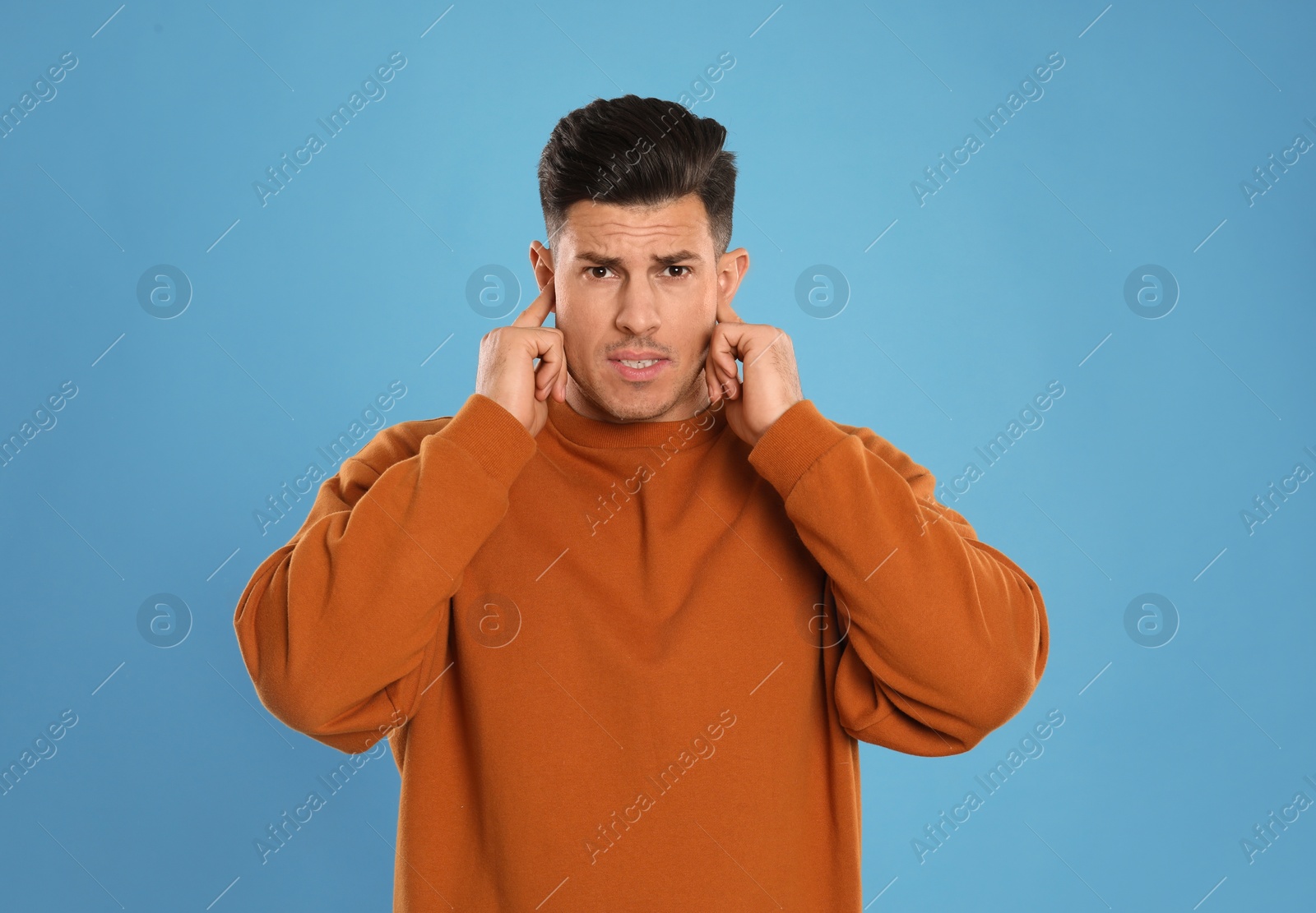 Photo of Man covering ears with fingers on light blue background