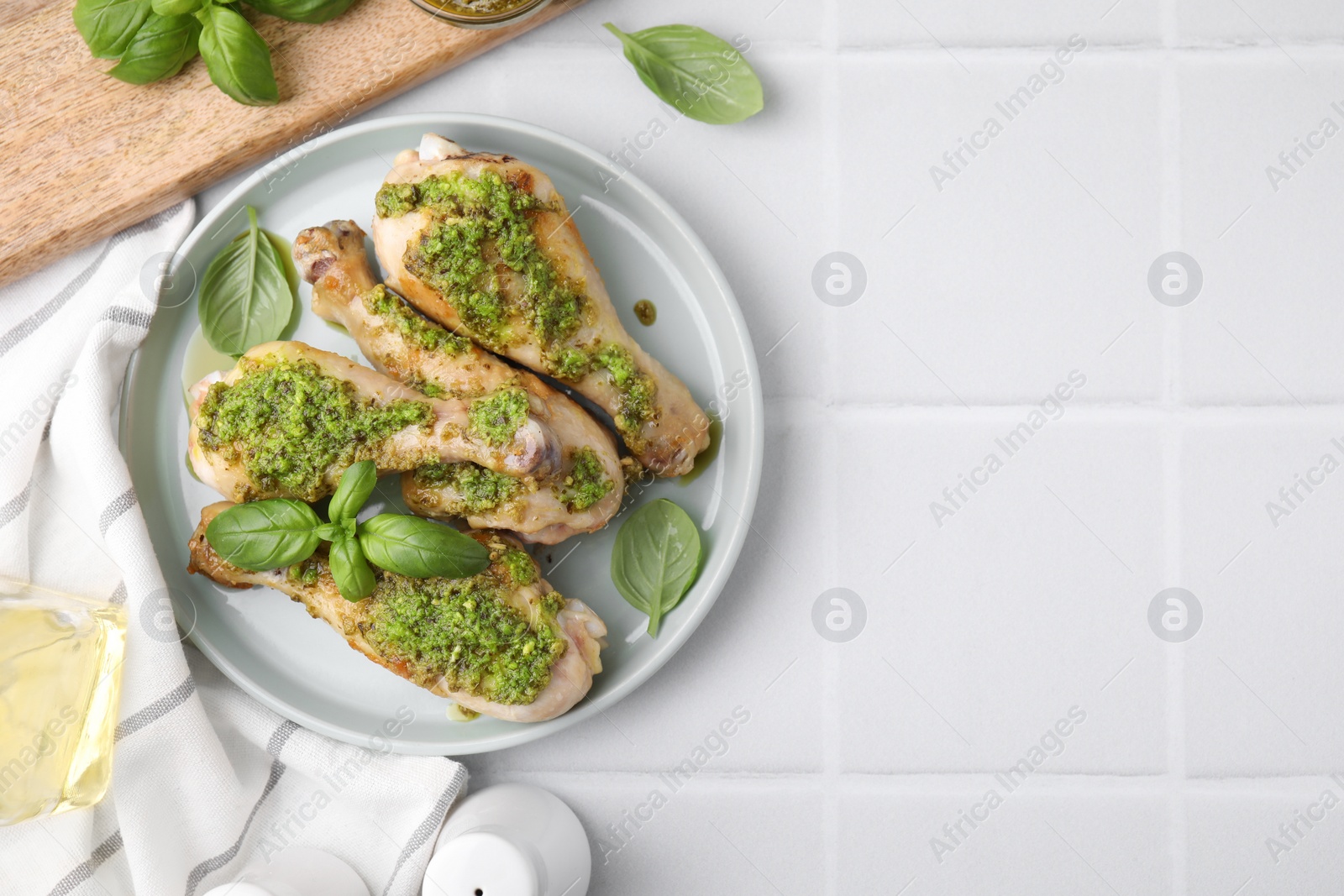 Photo of Delicious fried chicken drumsticks with pesto sauce and ingredients on white tiled table, flat lay. Space for text