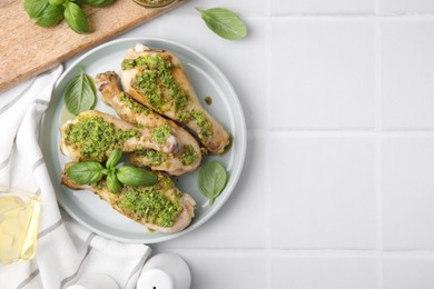 Delicious fried chicken drumsticks with pesto sauce and ingredients on white tiled table, flat lay. Space for text