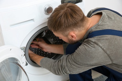 Young plumber fixing washing machine in bathroom