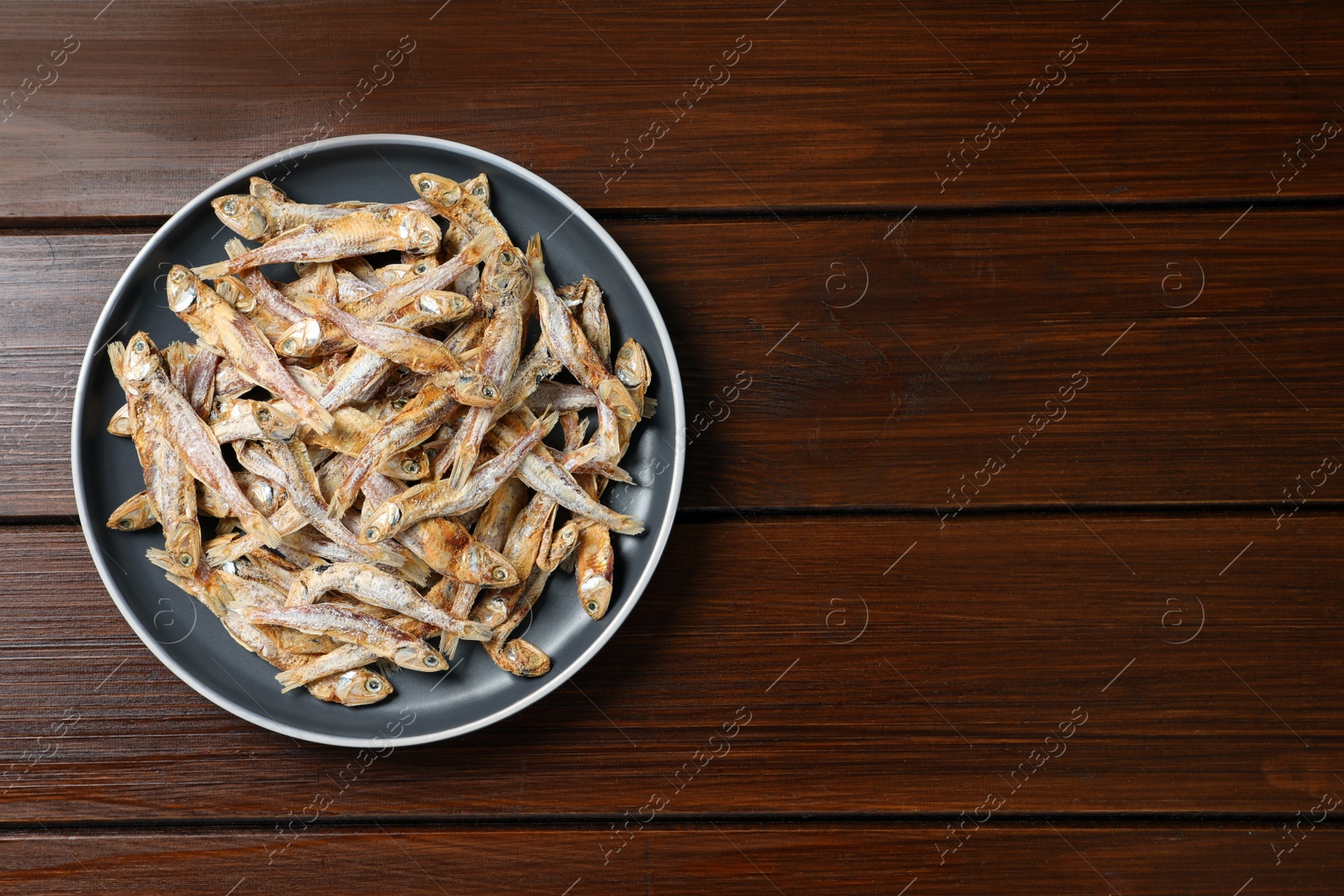 Photo of Plate of tasty dried anchovies on wooden table, top view. Space for text