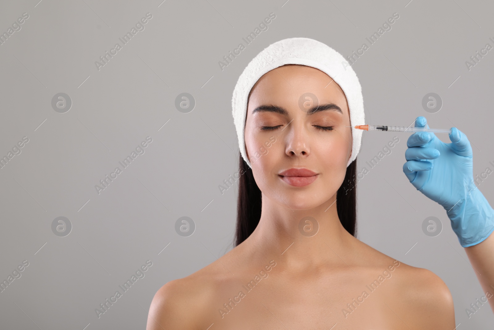 Photo of Doctor giving facial injection to young woman on light grey background, closeup. Cosmetic surgery