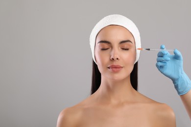 Doctor giving facial injection to young woman on light grey background, closeup. Cosmetic surgery