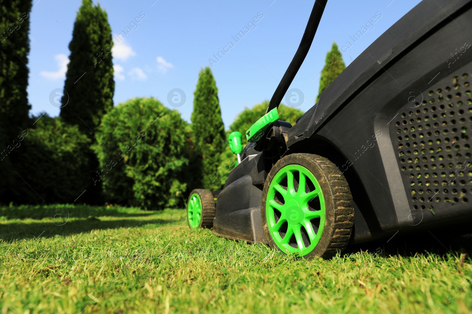 Photo of Lawn mower on green grass in garden, closeup. Space for text