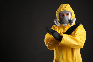 Photo of Man in chemical protective suit making stop gesture on black background, space for text. Virus research