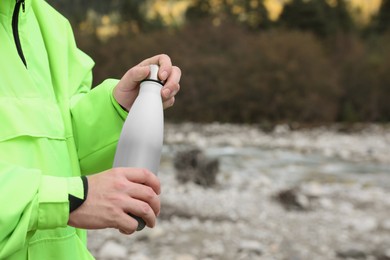 Woman holding thermo bottle in mountains, closeup. Space for text