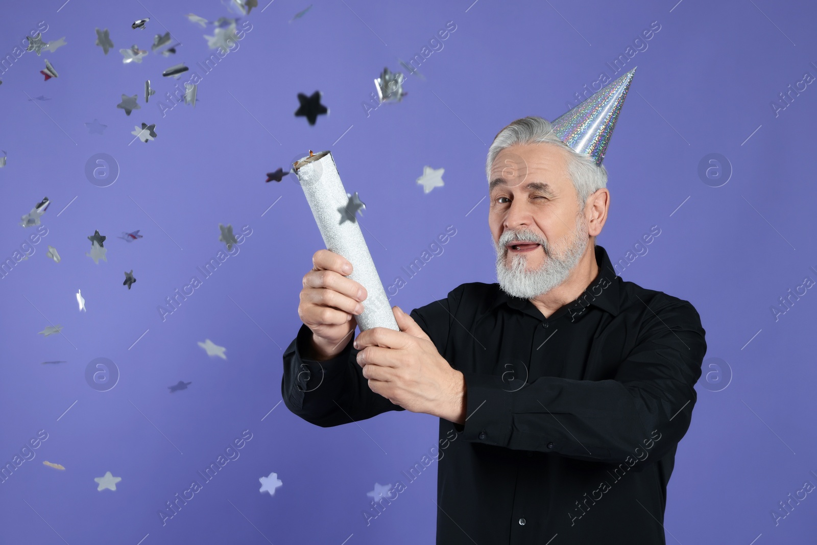 Photo of Man blowing up party popper and winking on purple background