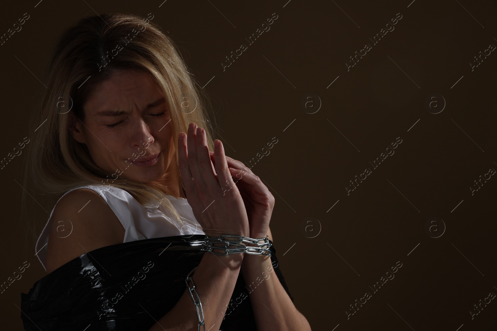 Photo of Scared woman taped up and taken hostage on dark background. Space for text