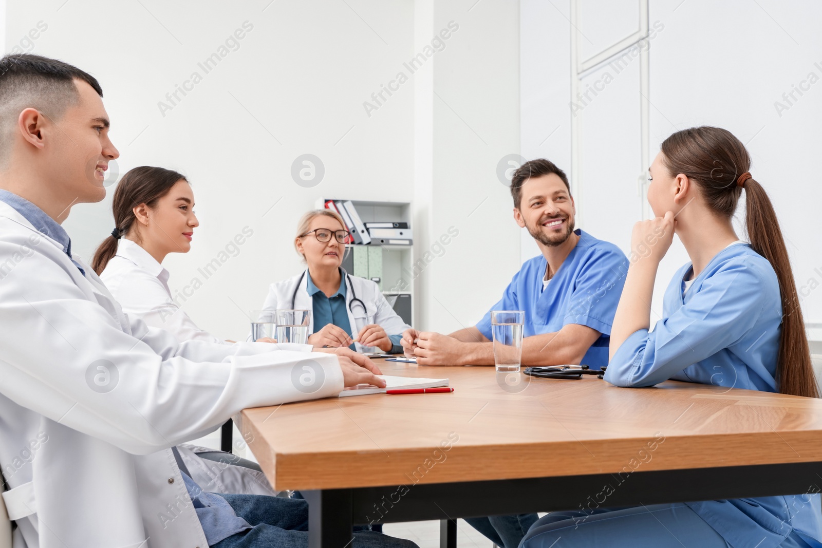 Photo of Medical conference. Team of doctors having discussion at wooden table in clinic