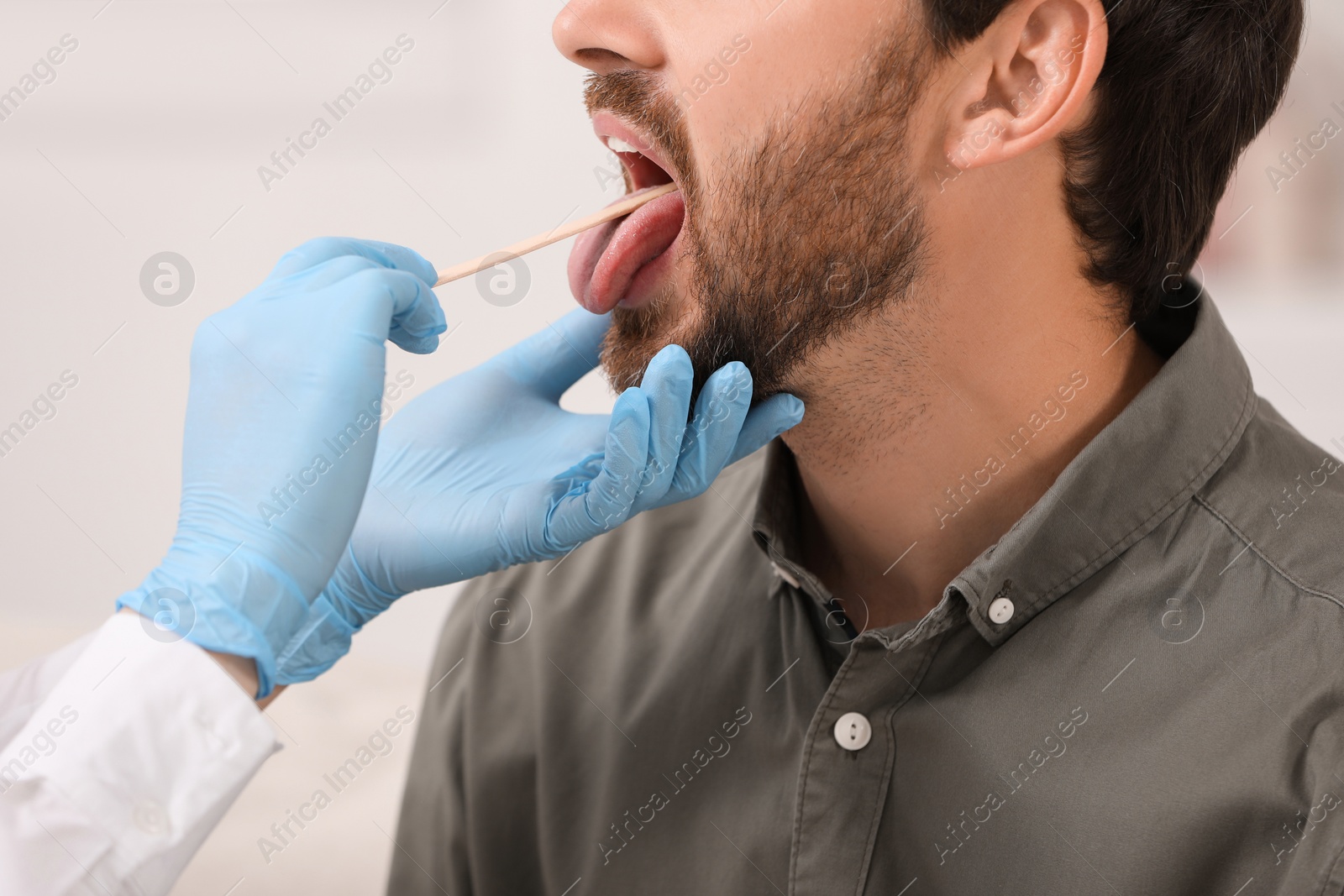 Photo of Doctor examining man`s oral cavity with tongue depressor on blurred background, closeup