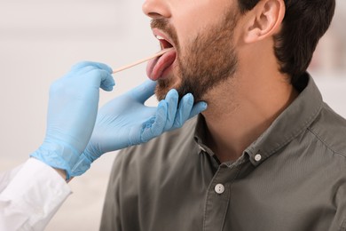 Photo of Doctor examining man`s oral cavity with tongue depressor on blurred background, closeup
