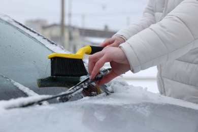 Photo of Man cleaning snow from car windshield outdoors, closeup