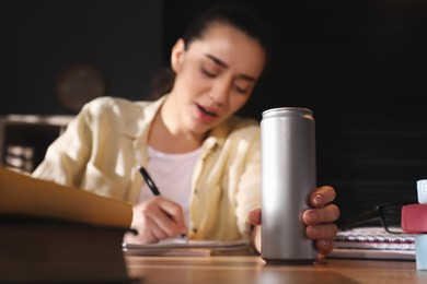Photo of Tired young woman with energy drink studying at home, focus on hand