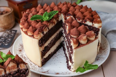 Photo of Delicious tiramisu cake with mint leaves on wooden table, closeup