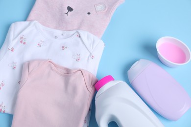 Photo of Laundry detergents and baby clothes on light blue background, flat lay