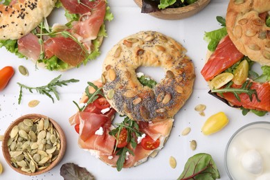 Tasty bagel sandwiches on white tiled table, flat lay