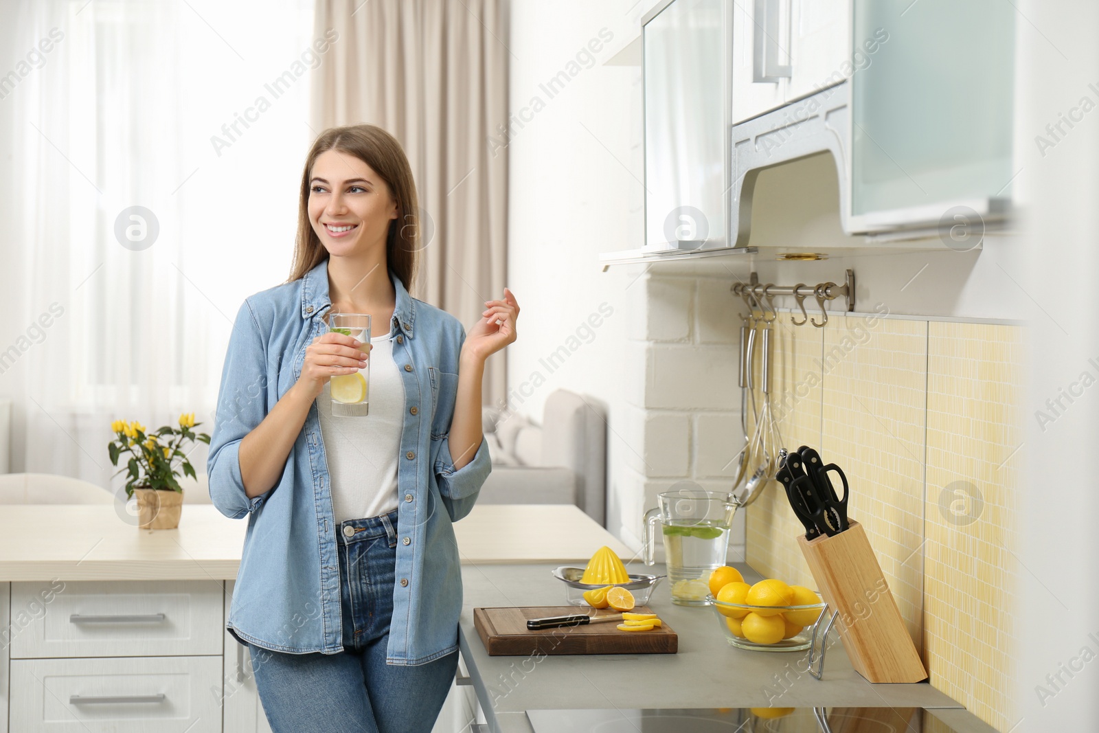 Photo of Young woman with glass of lemon water in kitchen