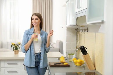 Young woman with glass of lemon water in kitchen
