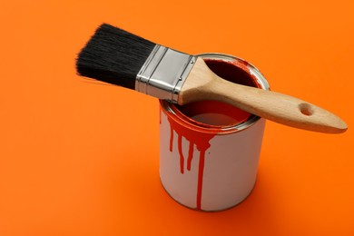 Photo of Can of orange paint and brush on color background