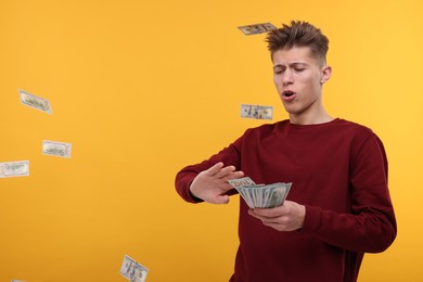 Handsome man throwing dollar banknotes on yellow background