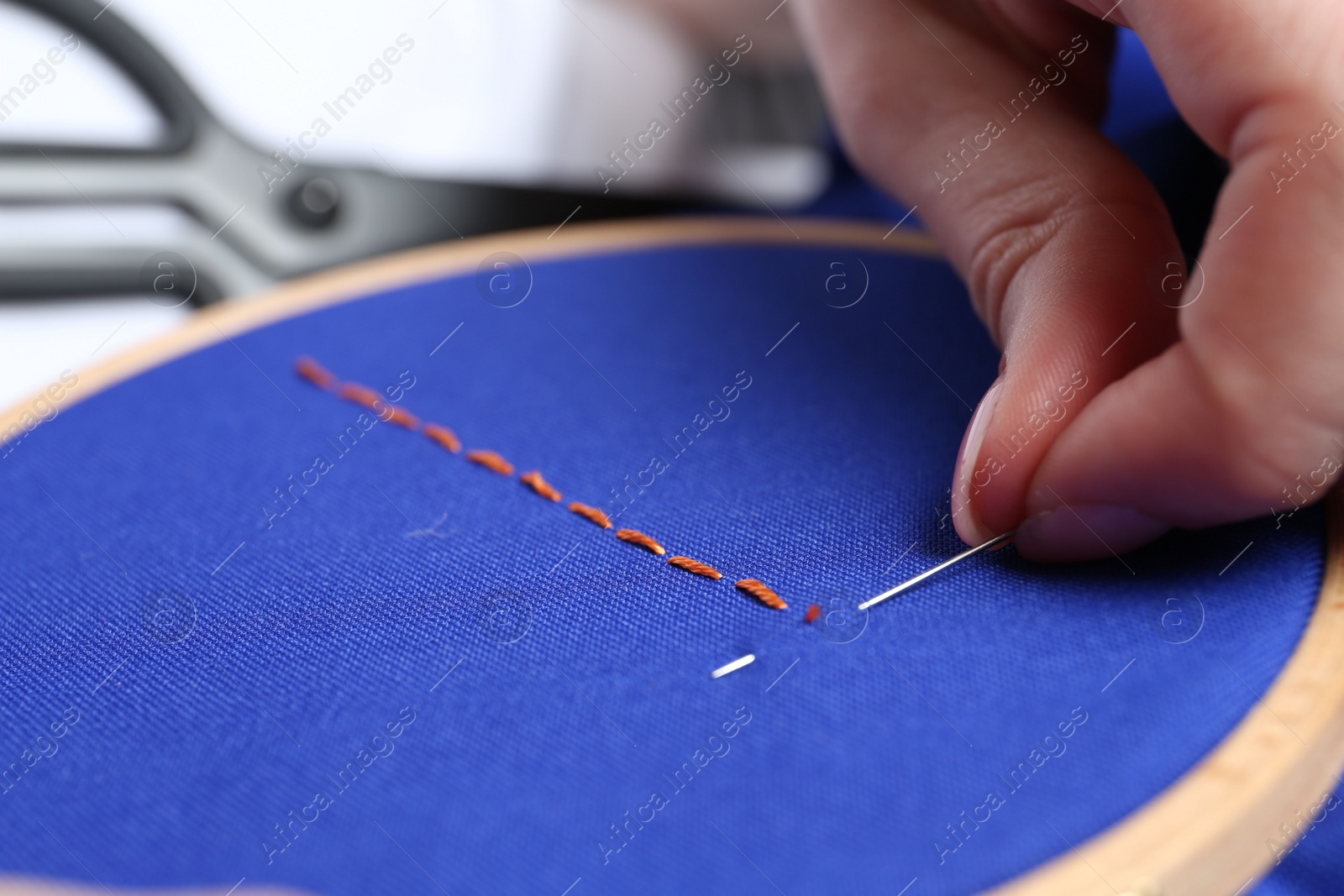 Photo of Woman with sewing needle and thread embroidering on cloth, closeup