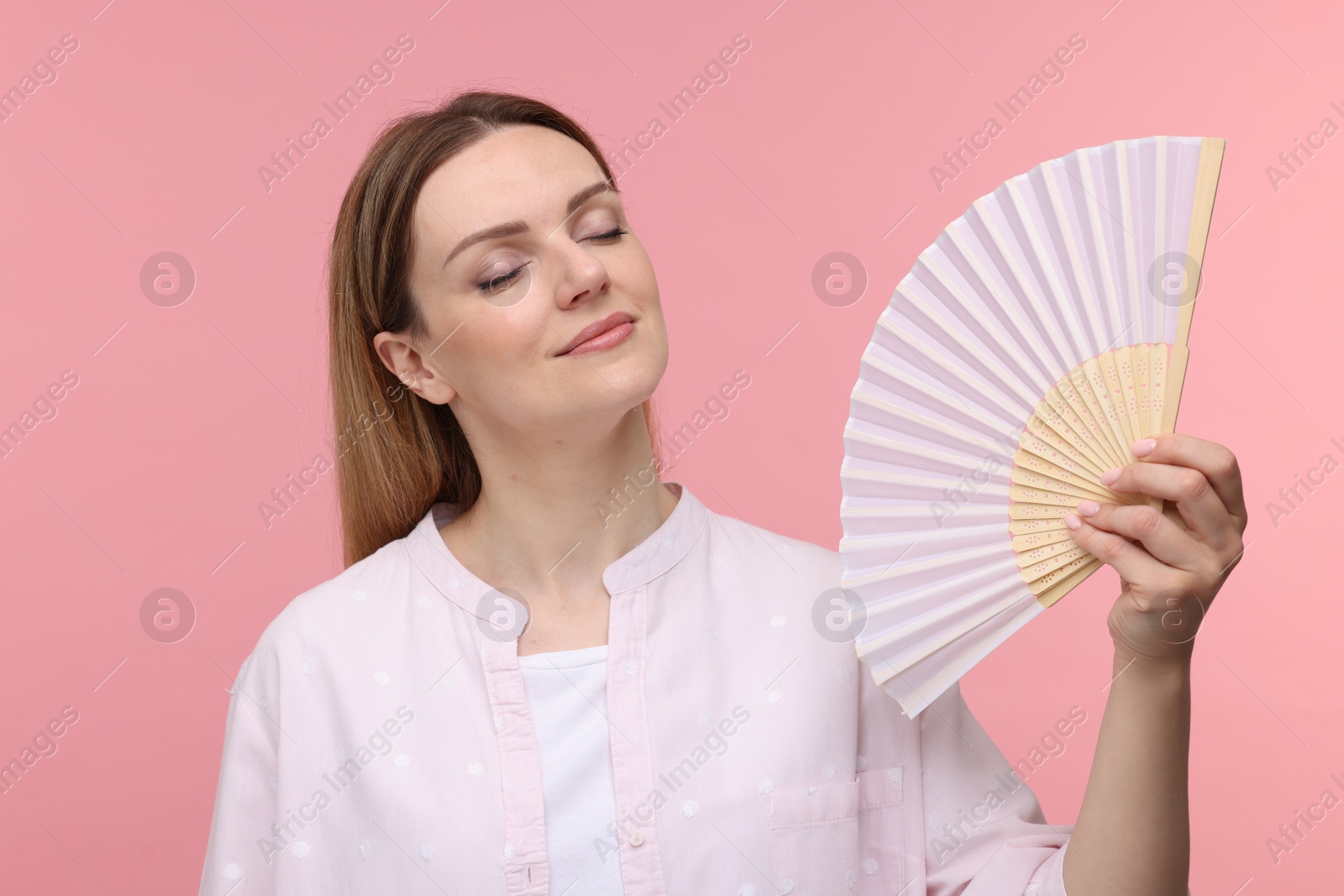 Photo of Beautiful woman waving hand fan to cool herself on pink background