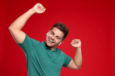 Photo of Happy young man listening to music through wireless earphones on red background