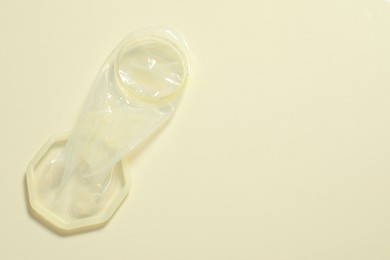 Photo of Unrolled female condom on beige background, top view and space for text. Safe sex