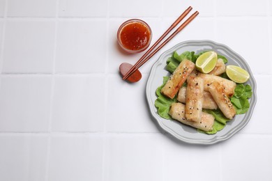 Photo of Tasty fried spring rolls served on white tiled table, flat lay. Space for text