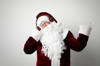 Photo of Santa Claus with headphones listening to Christmas music on light background