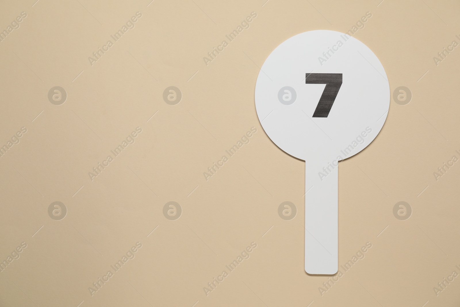 Photo of Auction paddle with number 7 on beige background, top view. Space for text