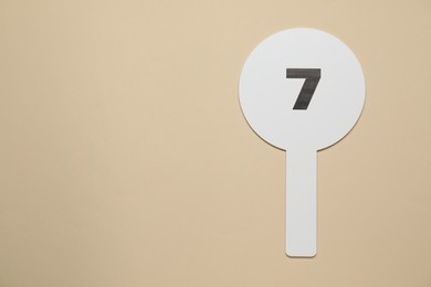 Photo of Auction paddle with number 7 on beige background, top view. Space for text