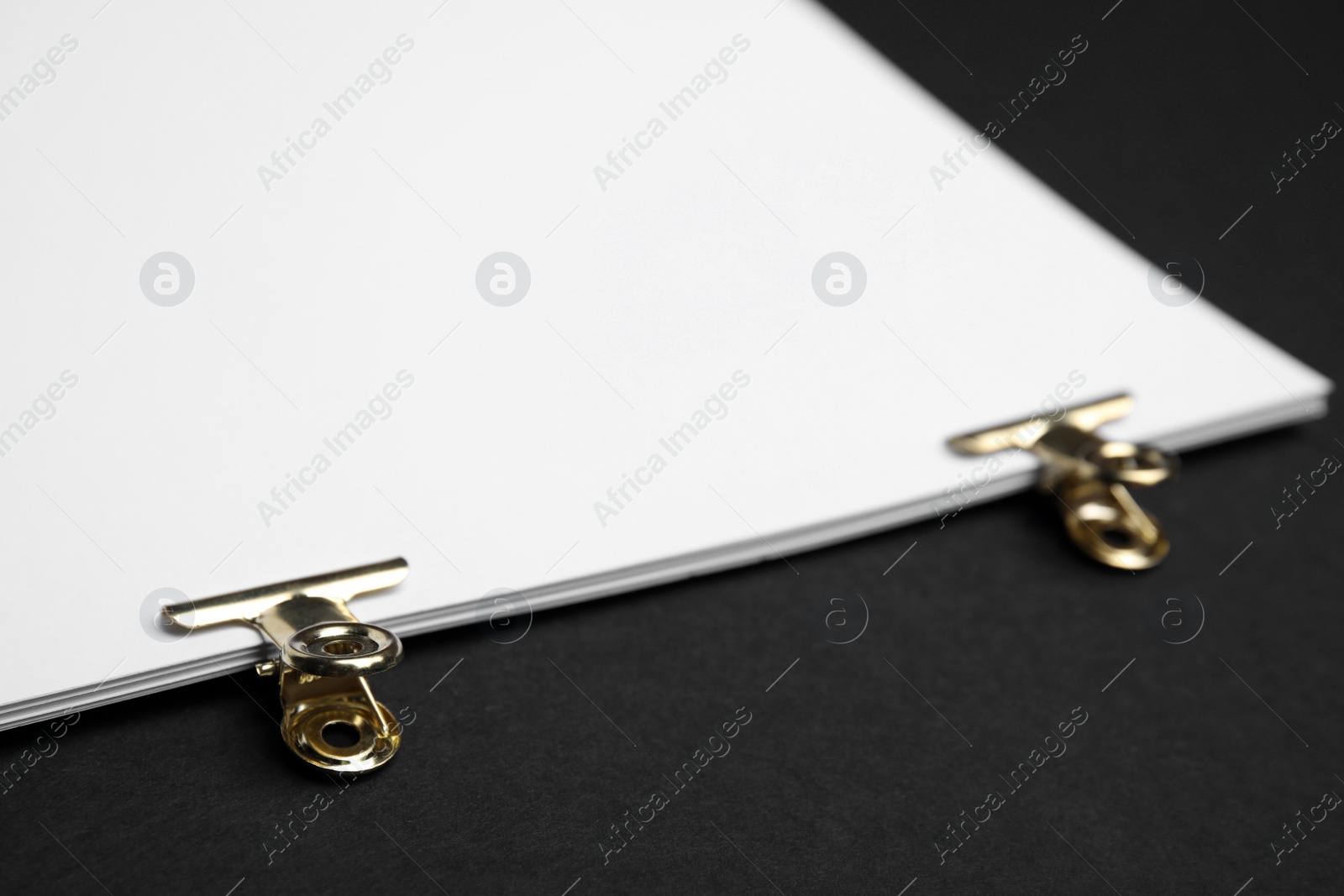 Photo of Sheets of paper with clips on black background, closeup