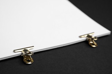 Photo of Sheets of paper with clips on black background, closeup