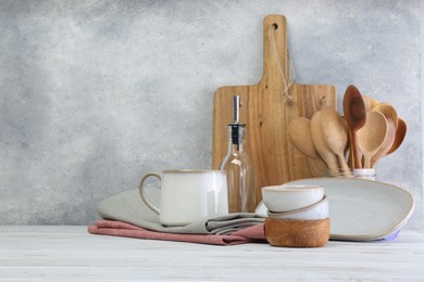 Different kitchenware and dishware on white wooden table against textured wall. Space for text
