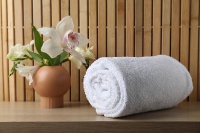 Photo of Rolled terry towel and beautiful flowers on wooden table