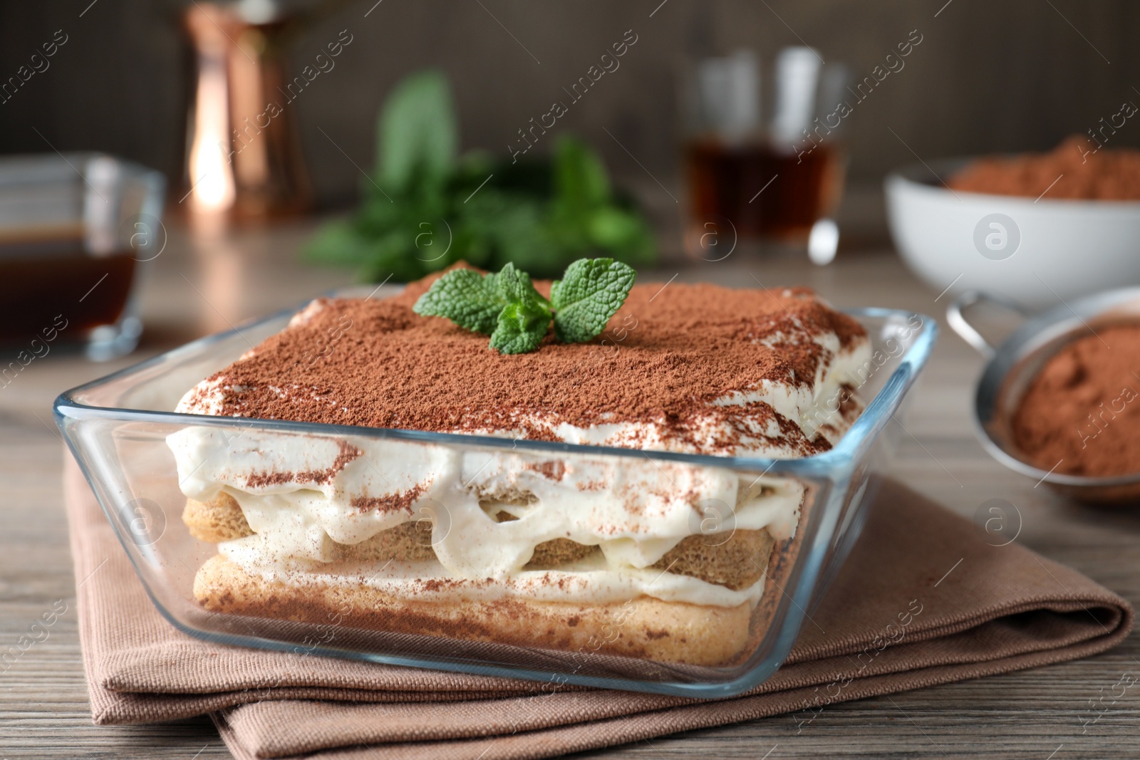 Photo of Glass bowl with delicious tiramisu cake on wooden table, closeup