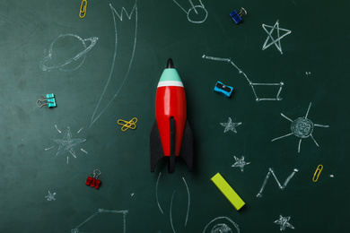 Photo of Bright toy rocket, school supplies and drawings on chalkboard, flat lay. Space for text