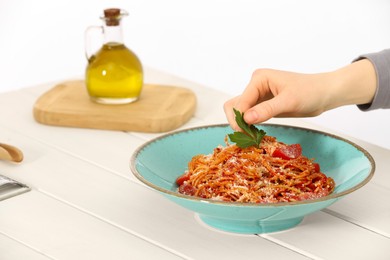 Photo of Food stylist decorating spaghetti with parsley at white wooden table in photo studio, closeup. Space for text