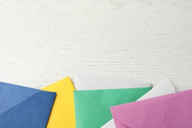 Colorful paper envelopes on white wooden background, flat lay. Space for text