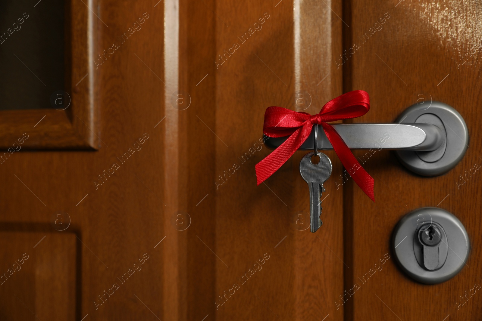 Photo of House key with red bow on door handle, closeup. Housewarming party