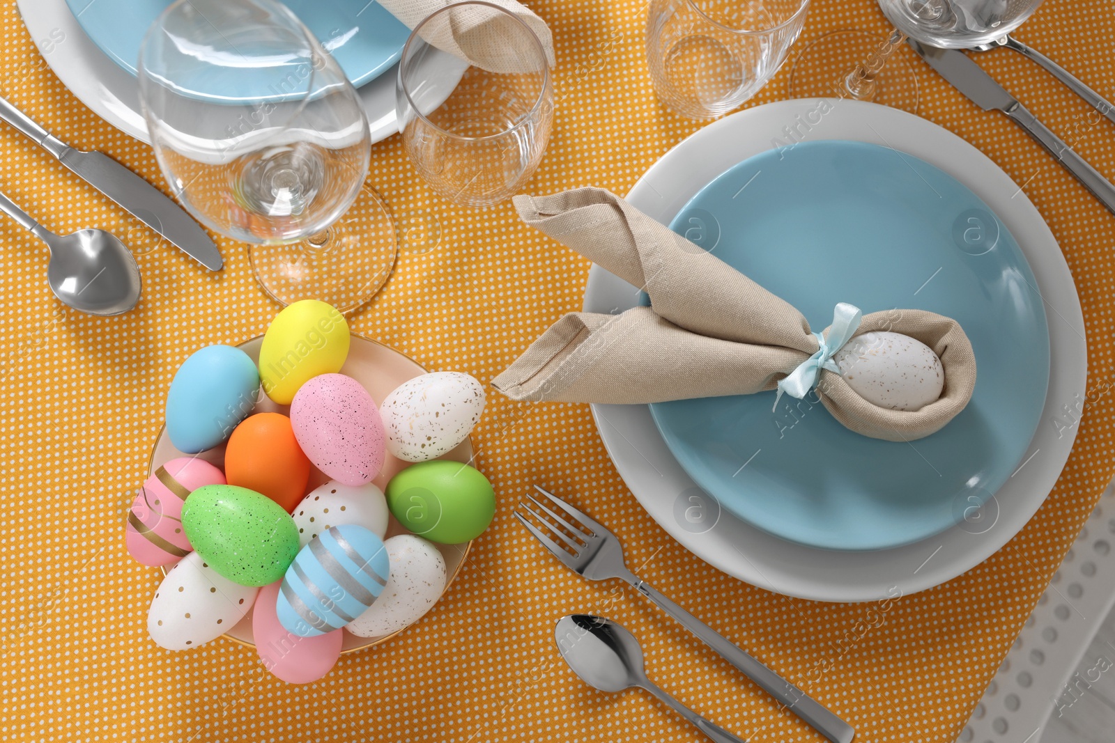 Photo of Festive table setting with painted eggs, plate and cutlery, flat lay. Easter celebration