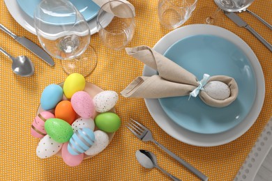 Photo of Festive table setting with painted eggs, plate and cutlery, flat lay. Easter celebration