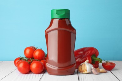 Photo of Bottle of tasty ketchup and ingredients on white wooden table