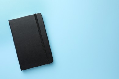 Photo of Closed black notebook on light blue background, top view. Space for text